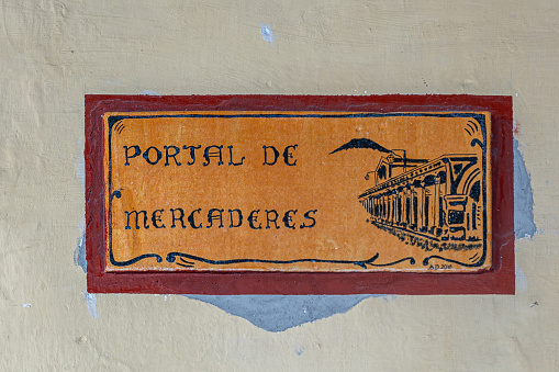 Guatemala, La Antigua - July 20, 2023: Portal de Mercaderes sign at entrance to shopping mall east side of Plaza Mayor, central square. Logo, emblem closeup, black om orange