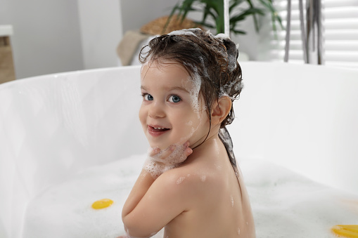 Cute little girl washing hair with shampoo in bathroom