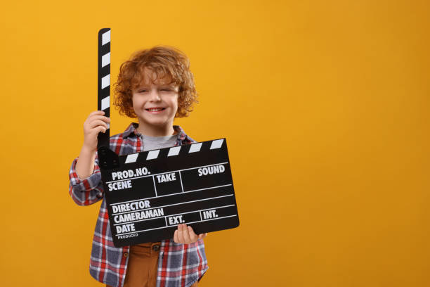 istock Smiling cute boy with clapperboard on orange background, space for text. Little actor 1773284990