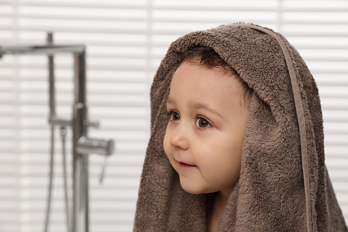 Cute little boy wrapped with towel after washing hair in bathroom. Space for text