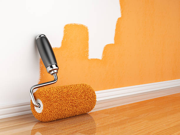 Incomplete orange wall painting with roller leaning on wall stock photo
