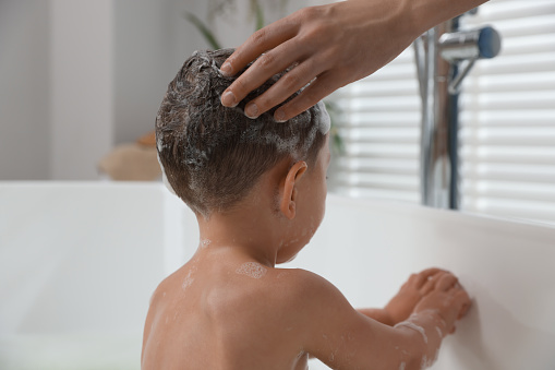 Mother washing her little son's hair with shampoo in bathroom