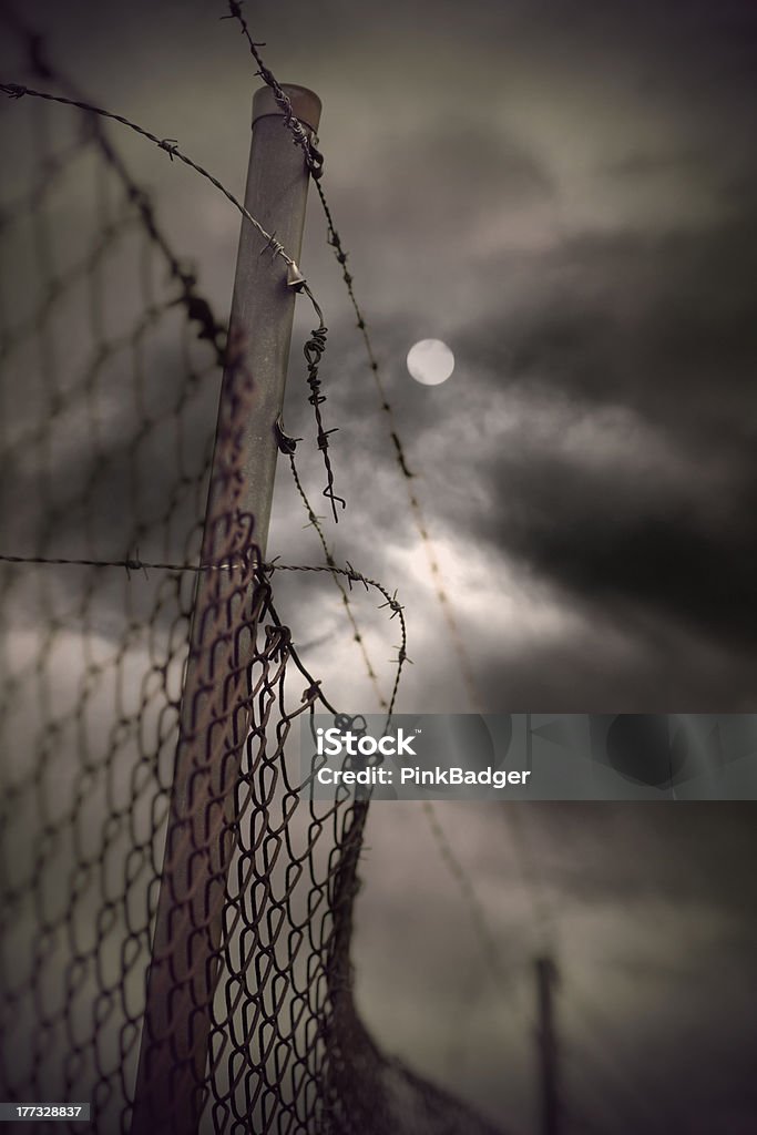 Barbed wire in evening Rusty barbed wire and chain link fence with vintage look on moody evening sky with moon Chainlink Fence Stock Photo