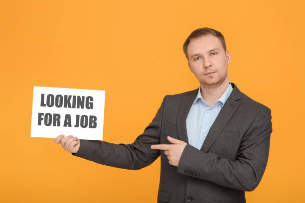 uomo disoccupato che indica il segno con la frase alla ricerca di un lavoro su sfondo arancione - lost occupation working orange foto e immagini stock
