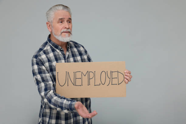 istock Confused senior man holding cardboard sign with word Unemployed on light grey background. Space for text 1773294412