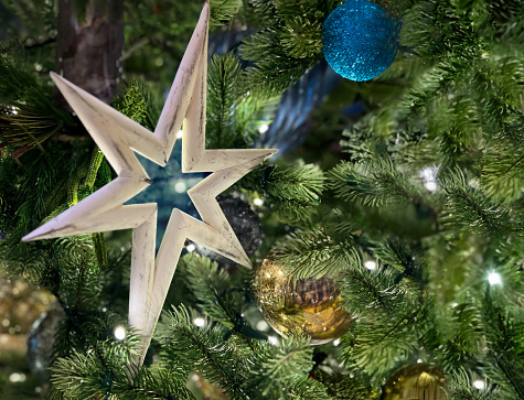 A white wood star decorates fan illuminated Christmas tree with gold and blue balls.