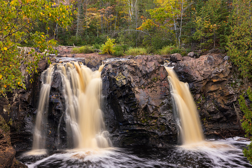 A scenic landscape featuring a twin waterfall in the woods during autumn.