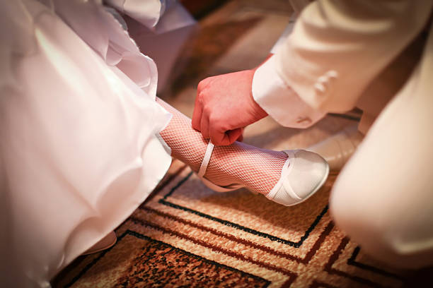 Groom in white costume is helping to wear classic wedding shoes on a bride before start of wedding ceremony.