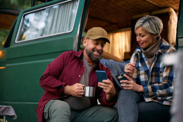 istock Happy couple using mobile phone by their camper trailer in the woods. 1773348555