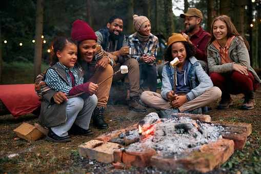 Two happy families enjoying in camping trip while roasting marshmallows on campfire in the woods.