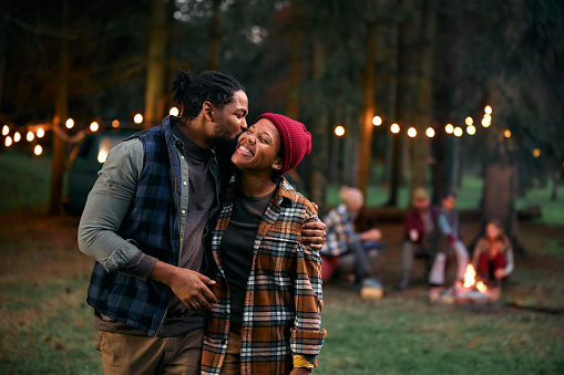 African American man kissing his wife while camping with their friends in nature.