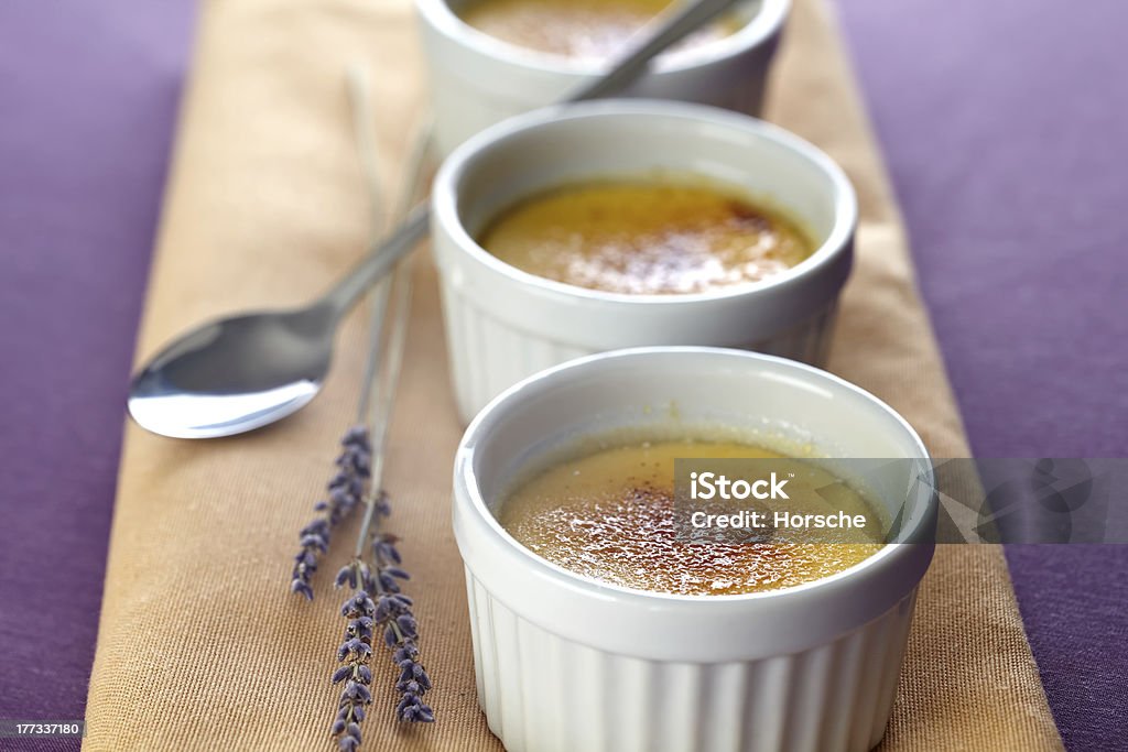 Cr&#232;me brulee with lavender Creme Brulee in three little baking moulds on a beige napkin placed on a violett tablecloth. Decorated with violet lavender blooms. Shallow depth of field. Baked Pastry Item Stock Photo
