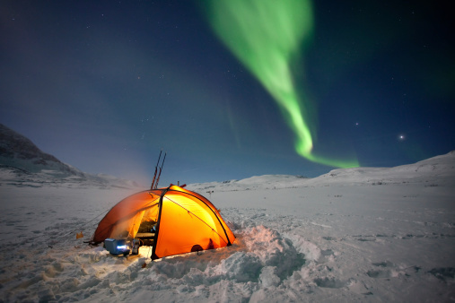 Northern Lights over a illuminatet Tent on a winterskitour in the North of Sweden