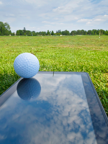 Golf ball on reflective mobile device, flat as a mat, at a driving range in summer