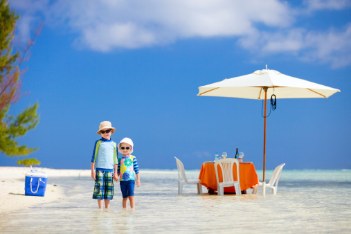 Two kids at picnic with table set in a shallow water near tropical beach