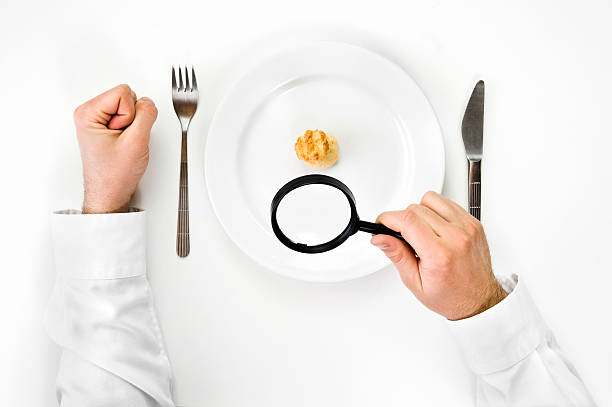Hunger and diet concept. Hand hold magnifying glass and enlarge small cake isolated from top view. big plate of food stock pictures, royalty-free photos & images
