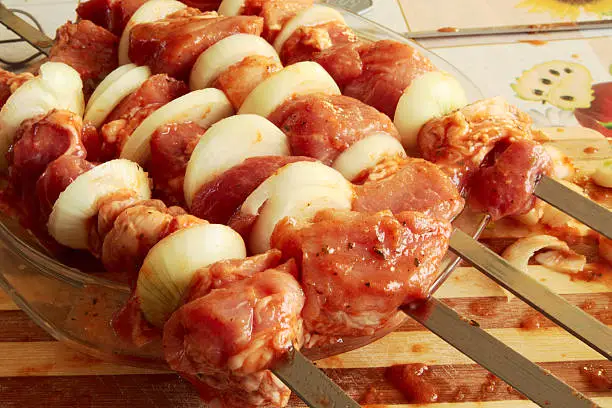 Raw meat with onion on skewers in a plate. Preparation of kebabs