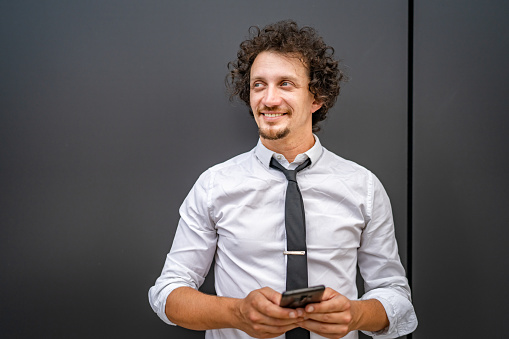 One caucasian man male businessman use smartphone mobile phone to make a call or send sms text messages texting online stand outdoor wear white shirt happy confident success real person copy space