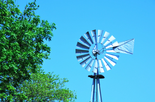 Silver windmill by green tree in front of blue sky.Click on the photo below to see my other photos of WINDMILLS . . .