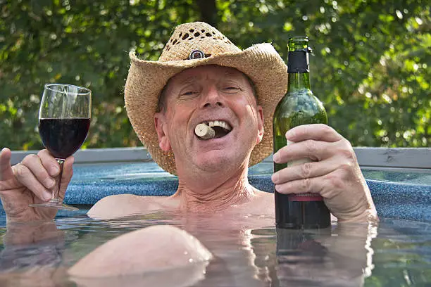 Photo of Man wearing cowboy hat sitting in hot tub with wine.