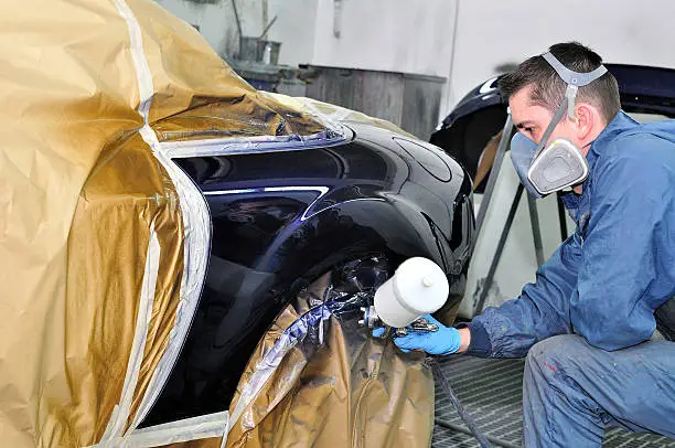 Man painting a car in a paint booth.