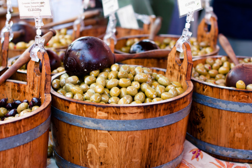 green olives in wooden barrel with black spoon for sale on a farmer's market.