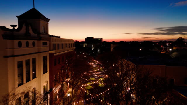 Hampton, VA twilight above street cafes in Downtown: parasols and string lights cover Queens Wy Street in sunset. Aerial footage with forward camera motion