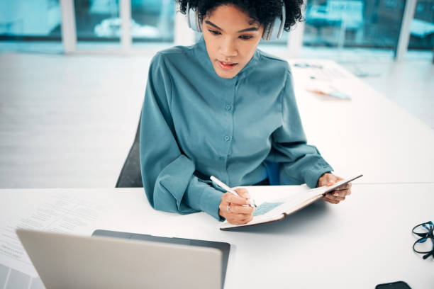 headphones, technology and woman writing notes in the office doing research for creative project. notebook, laptop and professional female designer working, planning and listen to music in workplace. - social housing audio imagens e fotografias de stock