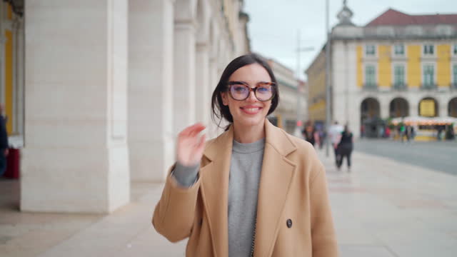 Woman in beige coat and glasses walking European city street