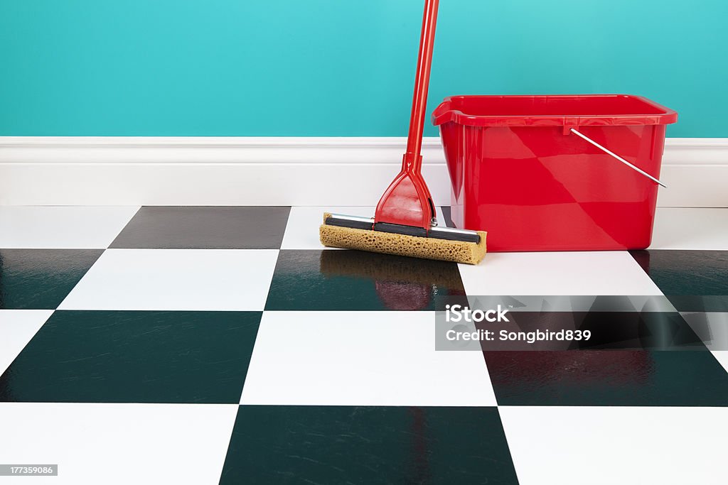 Mop and Bucket A red bucket and mop on a white and black checkered floor against a turquoise blue wall. Linoleum Stock Photo