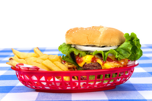 A freshly grilled cheeseburger in a red basket with freshly cooked french fries.