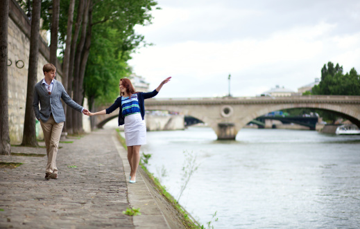 Couple is walking by the Seine embankment in Paris, girl is balancing on the water edge