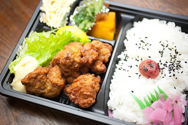 Japanese Cuisine Chicken Karaage Bento Bento is a single-portion takeout or home-packed meal common in Japanese cuisine. A traditional bento consists of rice, fish or meat, and one or more pickled or cooked vegetables, usually in a box-shaped container. Containers range from disposable mass produced to hand crafted lacquerware. Although bento are readily available in many places throughout Japan, including convenience stores, bento shops (弁当屋 bentō-ya), train stations, and department stores, it is still common for Japanese homemakers to spend time and energy for their spouse, child, or themselves producing a carefully prepared lunch box. packed lunch photos stock pictures, royalty-free photos & images