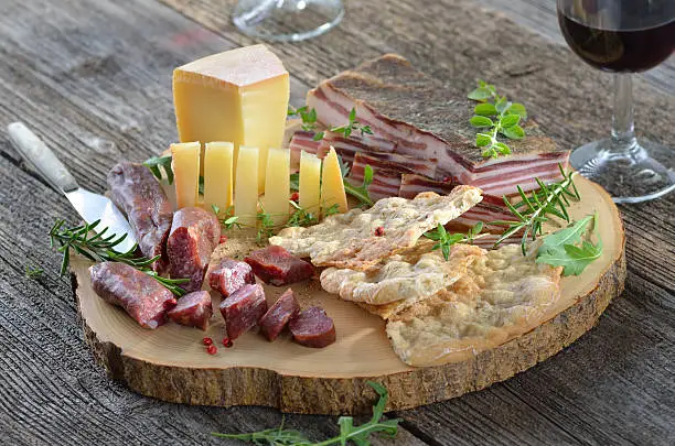Typical South Tyrolean snack with hearty cured bacon, mountain cheese, smoked sausages, crispy rye flatbread and a glass of red wine
