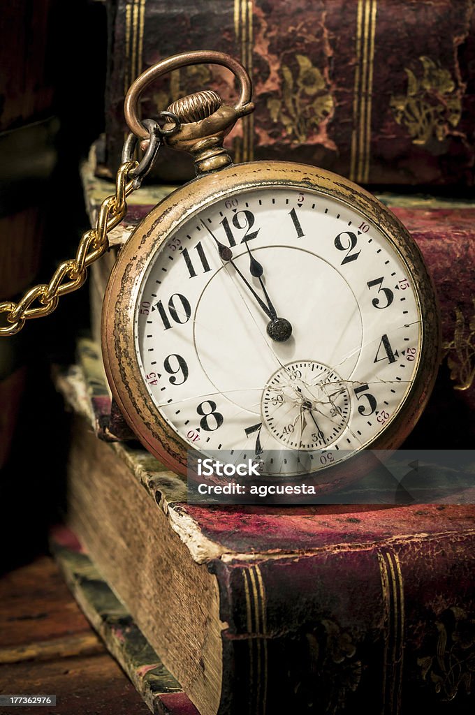 Old pocket watch and books in Low-key "Antique pocket clock showing a few minutes to midnight over ancient books in Low-key. Concept of time,the past or deadline." 12 O'Clock Stock Photo