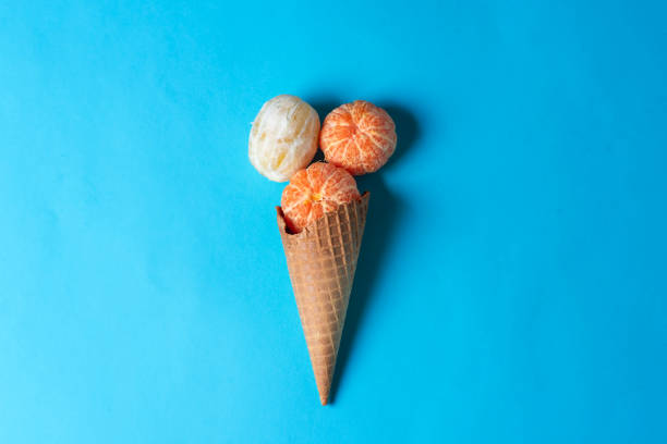 Ripe juicy tangerines and lemon in ice cream cone on a pastel blue background. Fruits, sweets and summer vacation concept. With copy space