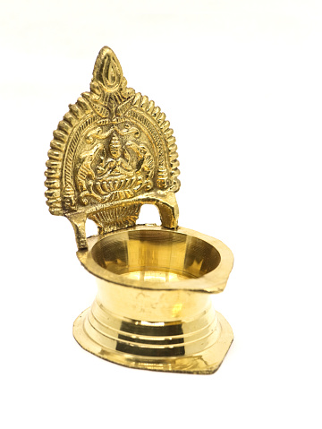 an antique brass kamatchi diya oil lamp with a hindu god carving used in traditional religious rituals for aarti pooja isolated in a white background