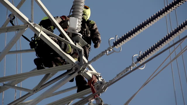 Tilt-down Reveal Of Linemen Working On Insulation String Of Transmission Tower. low angle