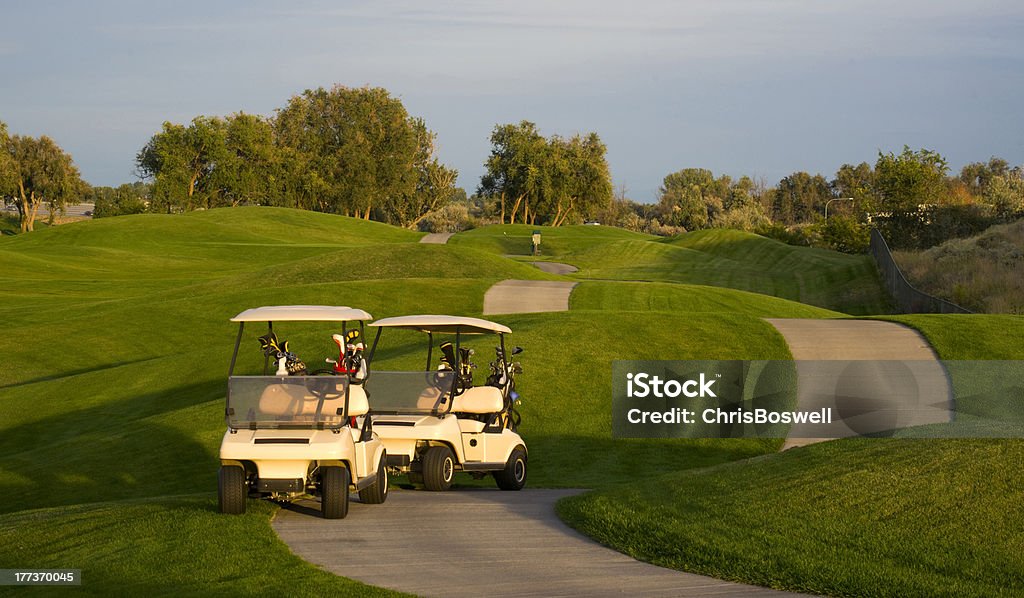 Pair of Golf Carts on the Green Course at Sunset Two golf carts stand on the path beside the ninth hole Country Club Stock Photo