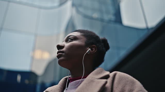 SLO MO Relaxed Businesswoman Listening To Music Through Headphones In Front Of Modern Office Building