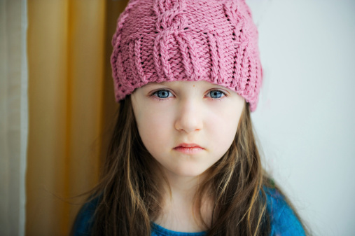 Close-up portrait of a sad child girl wearing pink knitted hat