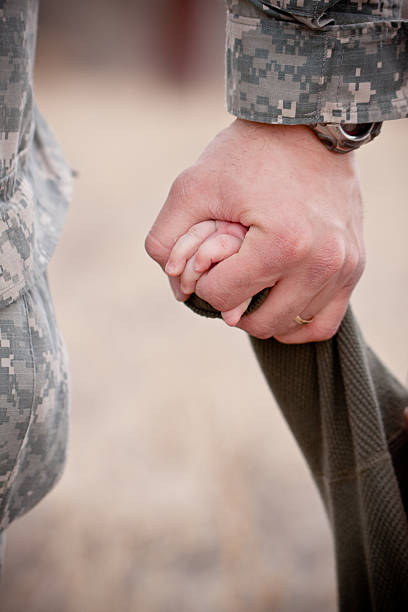 An adult hand in military fatigues holding a child's hand  Father and son holding hands military deployment photos stock pictures, royalty-free photos & images