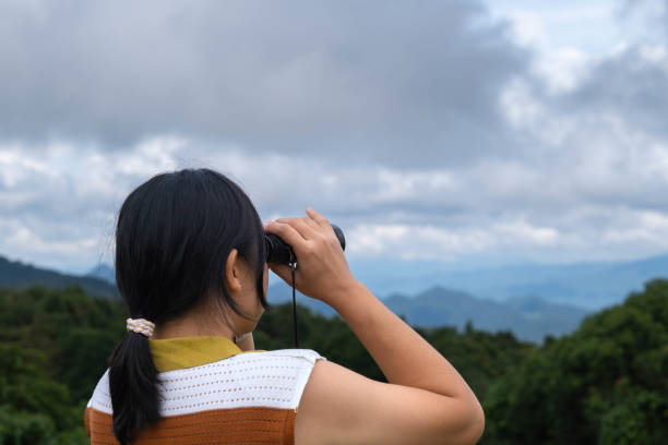 istock Young woman with binoculars on the mountain on a sunny day. Woman using binoculars when going hiking. Hiking woman uses binoculars to travel and has a happy smile. 1773802536