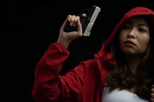 Asian Woman in Red Jacket holding the Short Gun in The Dark room, Criminal Society Concept