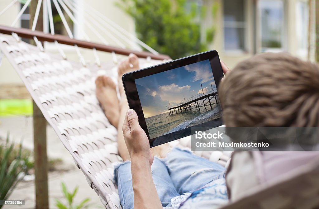 Man using  tablet computer while relaxing in a hammock Man using  tablet computer while relaxing in  hammock. Picture on the tablet pc screen - is part of my artwork. Digital Tablet Stock Photo