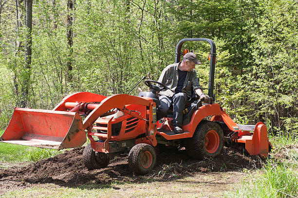 Tractor With Operator - Tilling An angled front view of a utility tractor tilling the soil with its operator in the open cab. garden tractor stock pictures, royalty-free photos & images