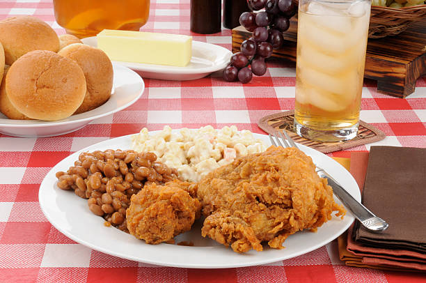 A plate of fried chicken with Boston baked beans and rolls on a picnic table on a summer day