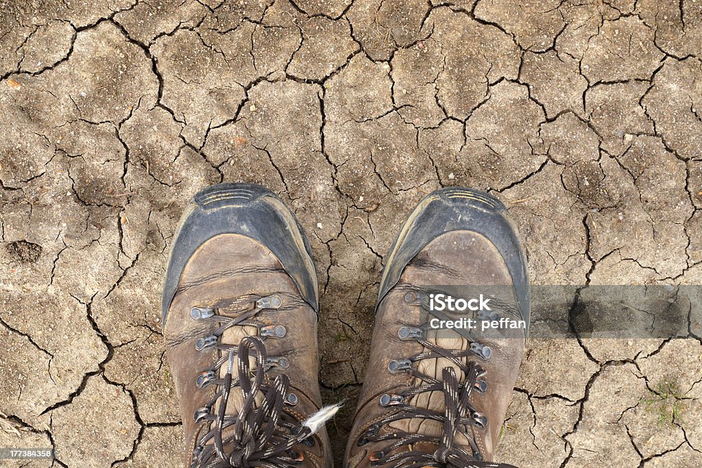 Hiking boots on dry desert soil "Young man walking the Way of St James, standing in his hiking boots on a dry desert soil in Castilla y LeAn, Spain" Hiking Boot Stock Photo