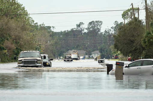 Flooded town street with moving cars submerged under water in Florida residential area after hurricane Ian landfall. Consequences of natural disaster.