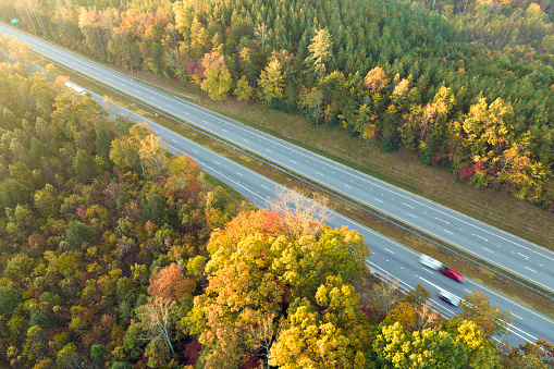 Aerial view of busy american highway with fast moving traffic surrounded by fall forest trees. Interstate transportation concept.